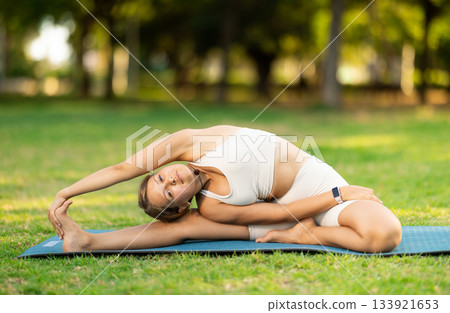 Girl in park on green grass of lawn performs Parivritta Janu Shirshasana Girl in park on green grass of lawn performs Parivritta Janu Shirshasana 133921653
