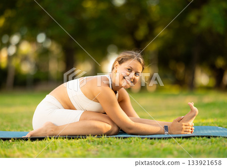 Girl in park on green grass of lawn performs Parivritta Janu Shirshasana Girl in park on green grass of lawn performs Parivritta Janu Shirshasana 133921658