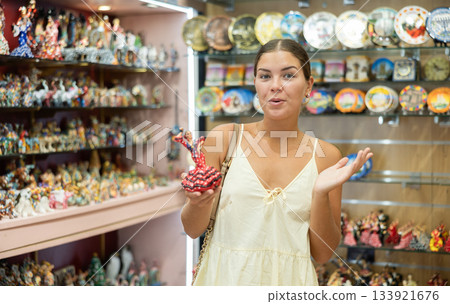 Female buyer holds in hands tests figurine she-dancer flamenco in memorable gifts shop Female buyer holds in hands tests figurine she-dancer flamenco in memorable gifts shop 133921676