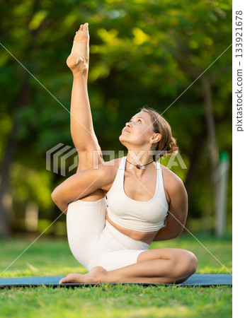 Girl in park on green grass of lawn performs Parivritta Surya Yantrasana Girl in park on green grass of lawn performs Parivritta Surya Yantrasana 133921678