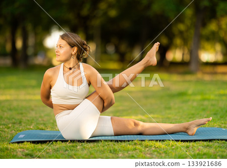 Girl in park on green grass of lawn performs eka padahastasana salamba navasana Girl in park on green grass of lawn performs eka padahastasana salamba navasana 133921686