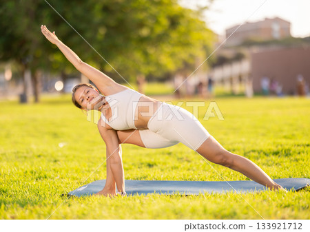 Girl doing Utthita Parsvakonasana yoga asana in summer park 133921712