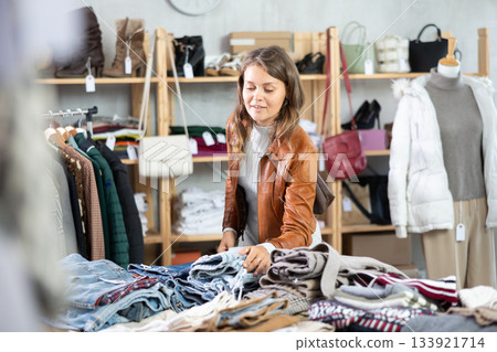 Happy young girl client carefully choosing stylish jeans trousers in clothing store. Winter sales concept Happy young girl client carefully choosing stylish jeans trousers in clothing store. Winter sales concept 133921714