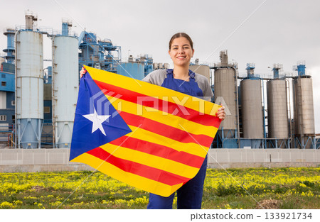 Smiling young woman near factory with Catalonia flag Smiling young woman near factory with Catalonia flag 133921734
