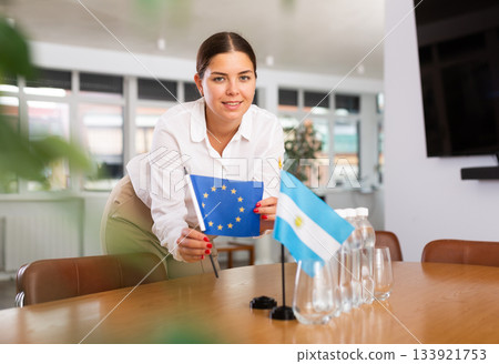 Positive young woman putting little flag of European Union on table next to the flag of Argentina Positive young woman putting little flag of European Union on table next to the flag of Argentina 133921753