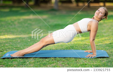 Fit girl performing Upward Plank Pose on green meadow 133921755