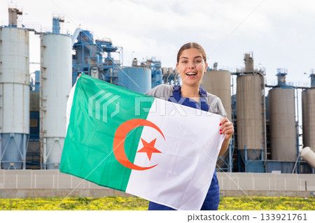 Smiling young woman near factory with Algeria flag Smiling young woman near factory with Algeria flag 133921761