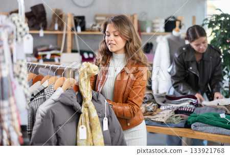 Uncertain young girl choosing something for autumn-winter in clothing store Uncertain young girl choosing something for autumn-winter in clothing store 133921768