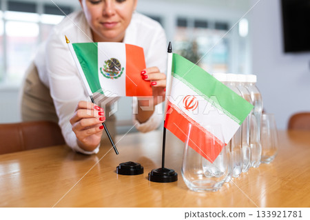 Little flag of Iran on table and flag of Mexico put next to it by young woman Little flag of Iran on table and flag of Mexico put next to it by young woman 133921781