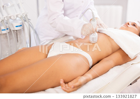 Aesthetician administering cold hammer therapy to tighten skin on female client belly Aesthetician administering cold hammer therapy to tighten skin on female client belly 133921827