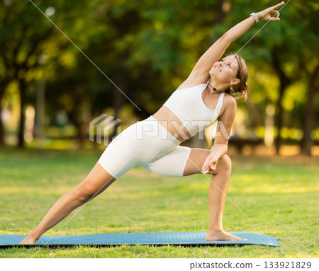 Girl in park on green grass of lawn performs Utthita Parshvakonasana 133921829
