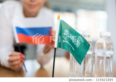 Little flag of Saudi Arabia on table and flag of Russia put next to it by young woman Little flag of Saudi Arabia on table and flag of Russia put next to it by young woman 133921895