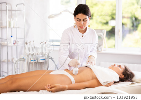 Cosmetologist performing cryotherapy procedure with cooling hammer on female client belly Cosmetologist performing cryotherapy procedure with cooling hammer on female client belly 133921955