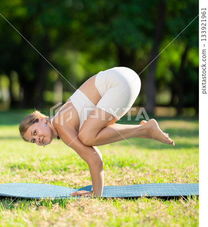 Smiling girl performing Bala Kakasana in green summer park 133921961