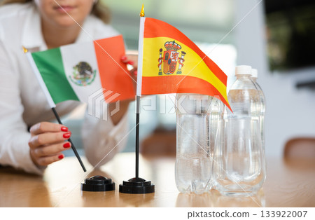 Young woman putting flags of Mexico and Spain on table in office Young woman putting flags of Mexico and Spain on table in office 133922007