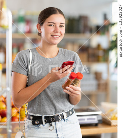 In shop youth girl scan QR code and take reading spices package bottle using phone camera 133922027