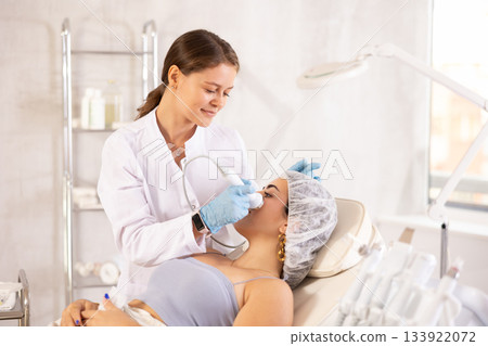 Cosmetologist performing facial procedure on woman using ultrasonic vibration attachment Cosmetologist performing facial procedure on woman using ultrasonic vibration attachment 133922072