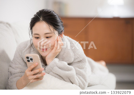 A young woman lying down in fluffy winter loungewear looking at her smartphone A young woman lying down in fluffy winter loungewear looking at her smartphone 133922079