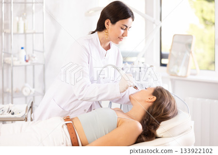 Cosmetologist performing facial procedure using ion bubble pen on female client 133922102