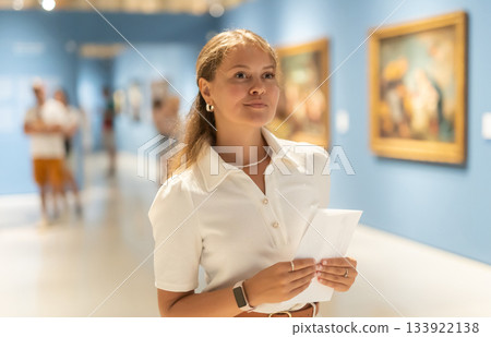 Woman with sheet piece of paper in hands view pictures and icons in museum hall Woman with sheet piece of paper in hands view pictures and icons in museum hall 133922138