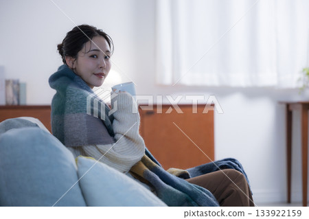 A young woman drinking a hot drink in a room with night lights. Winter image of a woman looking at the camera. 133922159
