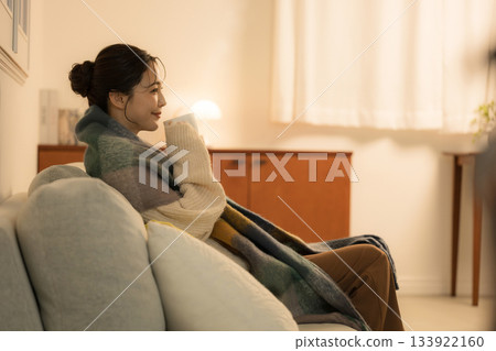 A young woman drinking a hot drink in a lit room at night. A winter image of a woman. A warm image of incandescent light. A young woman drinking a hot drink in a lit room at night. A winter image of a woman. A warm image of incandescent light. 133922160