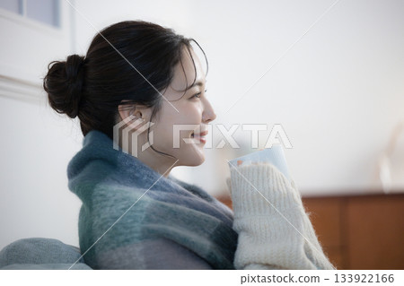 A young woman drinking a hot drink in a lit room at night. Winter image of a woman 133922166