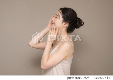 An image of a beautiful woman with her hair up and a beige background, easy to use for beauty and skin care, upper body, eyes closed with hands An image of a beautiful woman with her hair up and a beige background, easy to use for beauty and skin care, upper body, eyes closed with hands 133922315