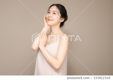 一位美麗女性的圖片,頭髮盤起,背景為米色,易於用於美容和護膚。上半身,雙手輕撫臉頰。 一位美麗女性的圖片,頭髮盤起,背景為米色,易於用於美容和護膚。上半身,雙手輕撫臉頰。 133922320