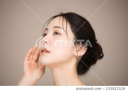 一位美麗女子,頭髮盤起,背景為米色,易於用於美容護膚,抬頭仰望。 一位美麗女子,頭髮盤起,背景為米色,易於用於美容護膚,抬頭仰望。 133922329