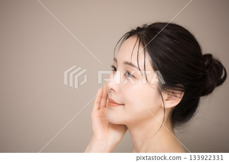 A close-up image of a beautiful woman with her hair up and a beige background, perfect for beauty and skincare 133922331