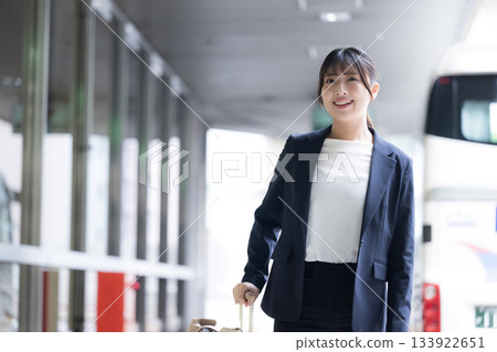 A woman in a suit with a suitcase at the airport or station. Business image of a business trip, upper body A woman in a suit with a suitcase at the airport or station. Business image of a business trip, upper body 133922651