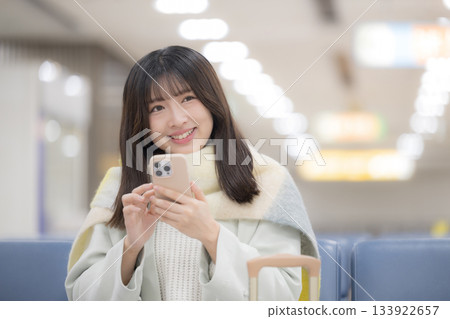 A woman operating a smartphone at an airport or station terminal 133922657