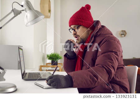 Freezing man sitting at desk blowing in his hands trying to keep warm Freezing man sitting at desk blowing in his hands trying to keep warm 133923131