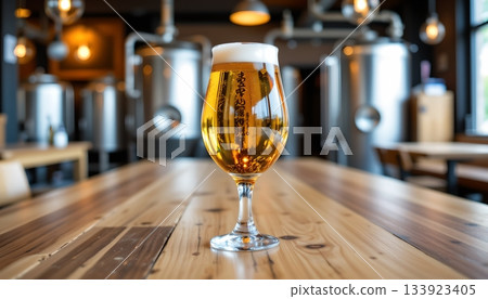 A wooden table in what appears to be a brewery setting with a rustic ambiance. A glass of beer is placed prominently on the table. 133923405