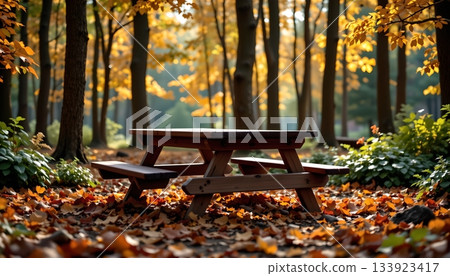 A serene autumnal park setting. In the center of the frame is a wooden picnic table, flanked by benches A serene autumnal park setting. In the center of the frame is a wooden picnic table, flanked by benches 133923417