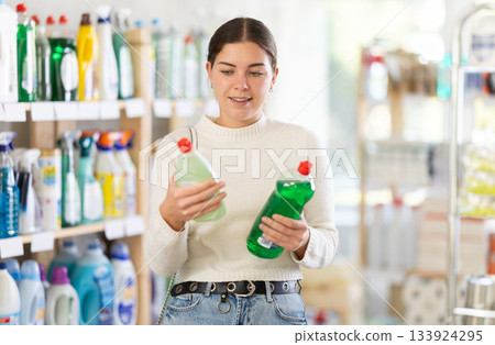 Girl housewife in household store examines package, chooses dishwashing Girl housewife in household store examines package, chooses dishwashing 133924295