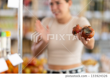 Woman holds rotten pomegranates in grocery store 133924326