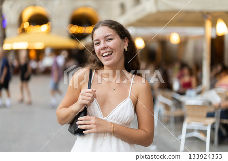 In evening, young smiling girl walks along city street Placa Real In evening, young smiling girl walks along city street Placa Real 133924353