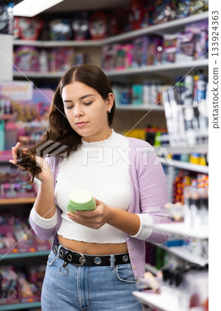 Portrait of positive woman looking on modern mousse for her hair in store. Portrait of positive woman looking on modern mousse for her hair in store. 133924363