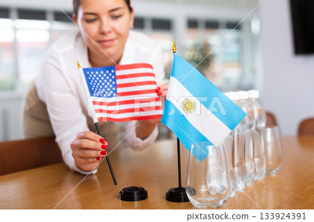 Little flag of Argentina on table and flag of the USA put next to it by young woman Little flag of Argentina on table and flag of the USA put next to it by young woman 133924391