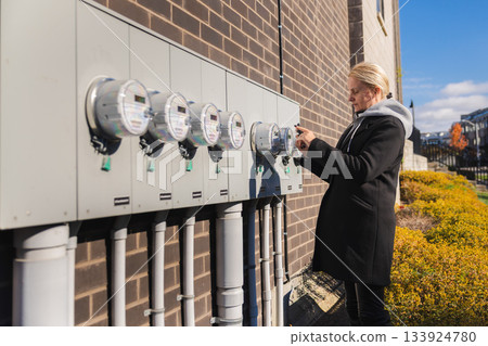 Woman checking outdoor electric utility meters on building wall in residential area 133924780