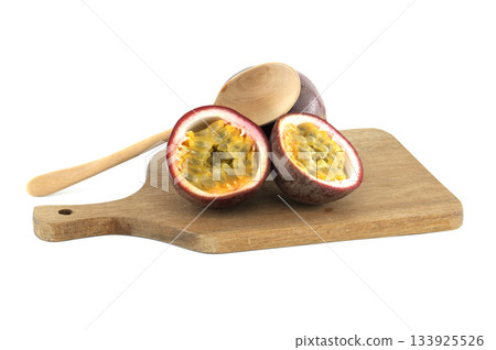 Fresh passion fruits cut in half showing the pulp and seeds, lying on wooden cutting board with wooden spoon Fresh passion fruits cut in half showing the pulp and seeds, lying on wooden cutting board with wooden spoon 133925526