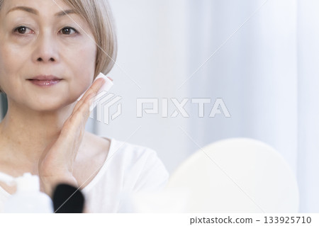 Senior woman putting on makeup by a bright window 133925710