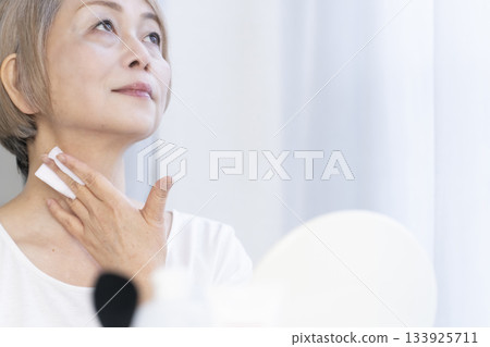 Senior woman putting on makeup by a bright window 133925711