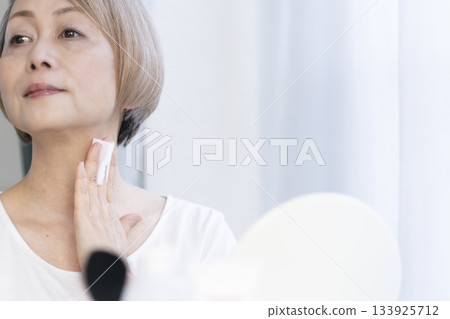 Senior woman putting on makeup by a bright window 133925712