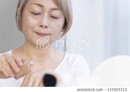 Senior woman putting on makeup by a bright window 133925713