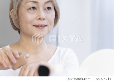 Senior woman putting on makeup by a bright window 133925714