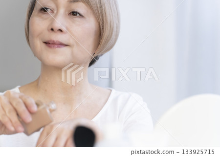 Senior woman putting on makeup by a bright window 133925715