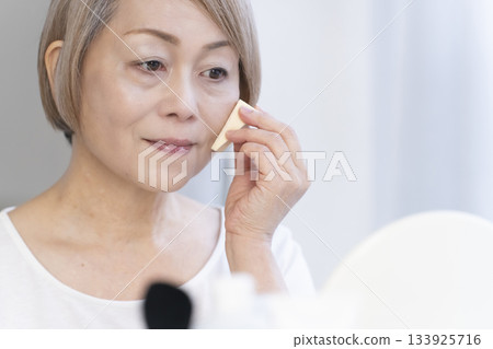Senior woman putting on makeup by a bright window 133925716